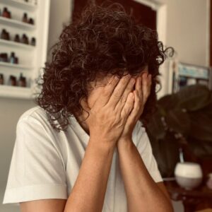 Theoni Papoutsis hands covers her face, sitting at desk, overwhlemed